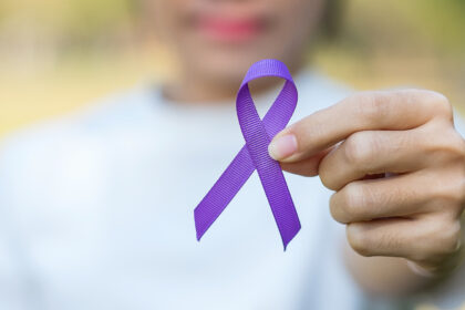 Pessoa segurando o laço roxo, símbolo da campanha Fevereiro Roxo de conscientização sobre lúpus, fibromialgia e Alzheimer.
