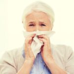 Pessoa idosa com sintomas gripais, com lenço no rosto.