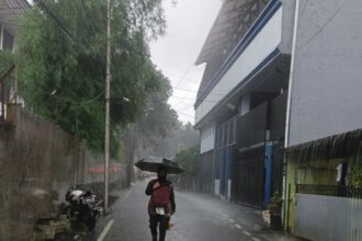 Pessoa caminha sob chuva intensa em área alagada, representando riscos à saúde durante o período chuvoso