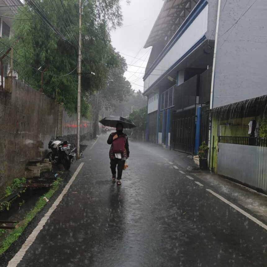 Pessoa caminha sob chuva intensa em área alagada, representando riscos à saúde durante o período chuvoso
