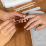 Profissional realizando procedimento de manicure com instrumentos metálicos em salão de beleza.