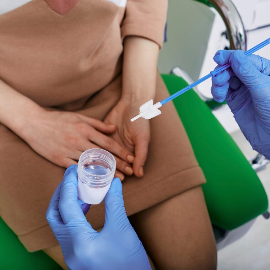 Profissional com luvas segura escova ginecológica e frasco coletor durante procedimento de exame preventivo do colo do útero em consultório médico.