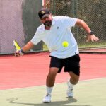 Homem jogando tênis em quadra durante partida com foco na movimentação e preparo físico