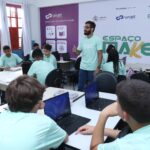 Alunos da rede pública participando de aula de robótica com notebooks em espaço maker educativo