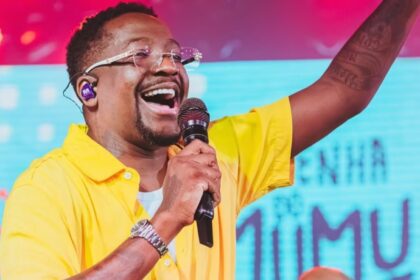 Cantor Mumuzinho se apresenta no palco durante show da turnê Resenha do Mumu, com público e estrutura de evento musical ao fundo
