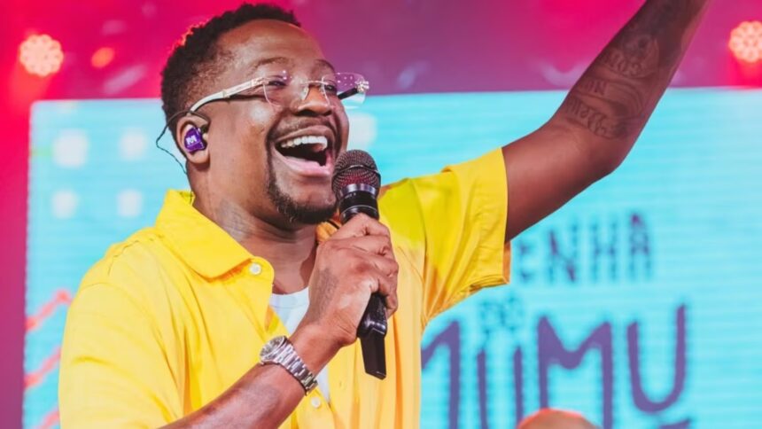 Cantor Mumuzinho se apresenta no palco durante show da turnê Resenha do Mumu, com público e estrutura de evento musical ao fundo
