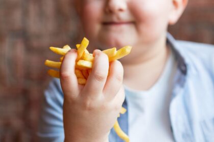 Criança segurando alimentos industrializados em contraste com frutas, em alerta para obesidade infantil causada por ultraprocessados.