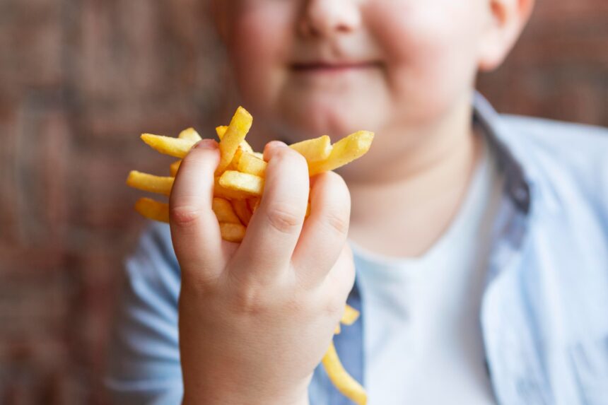 Criança segurando alimentos industrializados em contraste com frutas, em alerta para obesidade infantil causada por ultraprocessados.