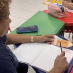 Grupo de alunos adultos participa de aula de alfabetização em sala de ensino, acompanhados por instrutores durante atividade de leitura e escrita em Ananindeua.
