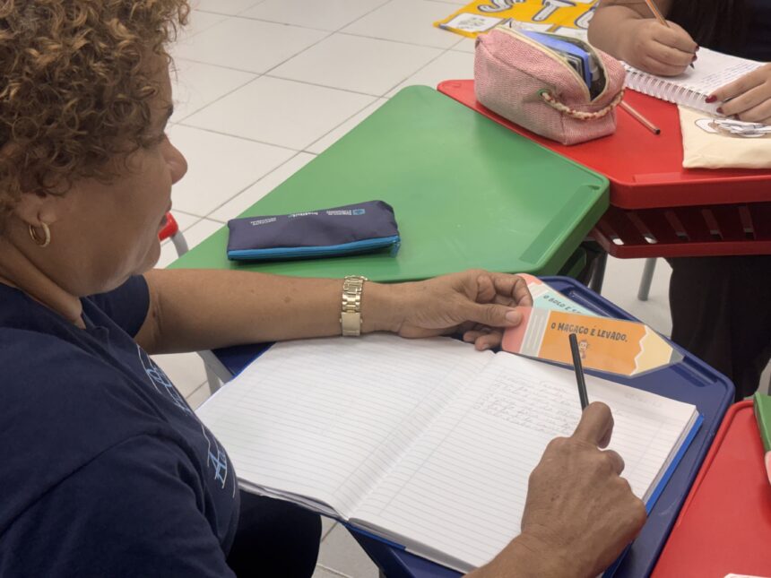 Grupo de alunos adultos participa de aula de alfabetização em sala de ensino, acompanhados por instrutores durante atividade de leitura e escrita em Ananindeua.