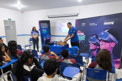 Alunos sentados em sala de aula acompanham apresentação sobre tecnologia e sustentabilidade enquanto educadores demonstram equipamentos de realidade virtual em escola pública.
