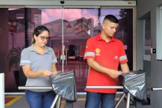 Mãe e filho passam juntos pela catraca de acesso de uma fábrica em Belém, usando uniforme da empresa durante a rotina de trabalho.
