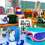 Vasos artesanais coloridos com pinturas decorativas e pequenas plantas expostos em feira de artesanato e jardinagem em Fortaleza.