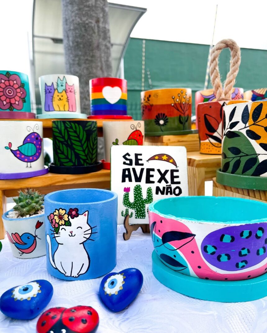 Vasos artesanais coloridos com pinturas decorativas e pequenas plantas expostos em feira de artesanato e jardinagem em Fortaleza.